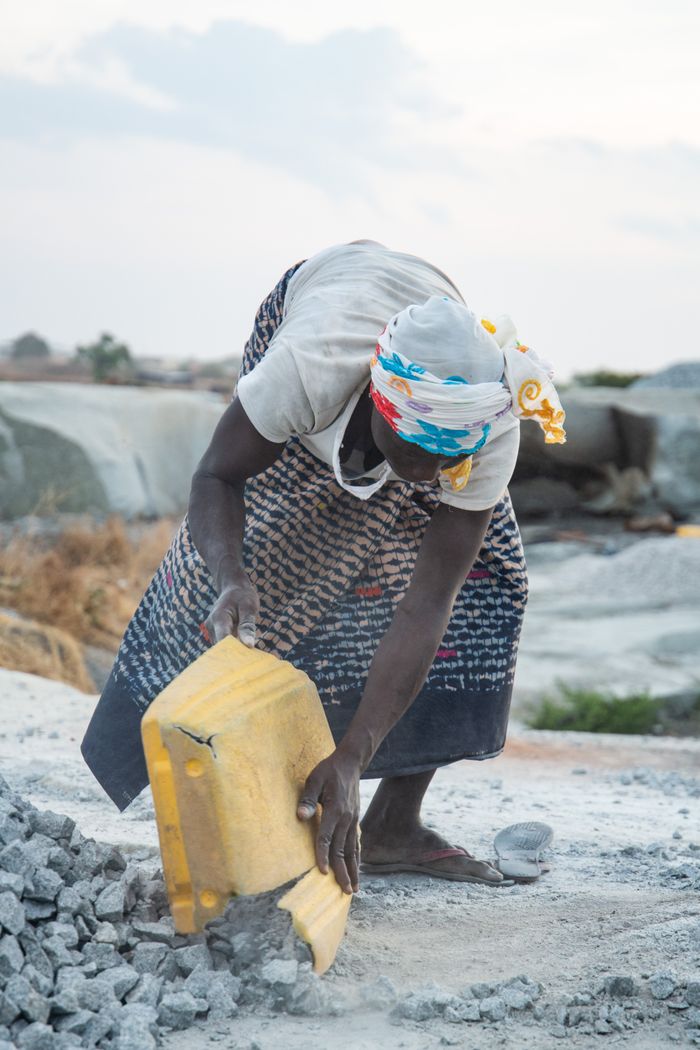 An African woman works tirelessly moving rocks at a quarry site outdoors.